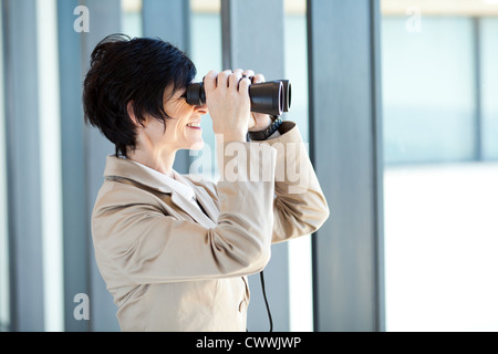middle aged businesswoman using binoculars in office Stock Photo