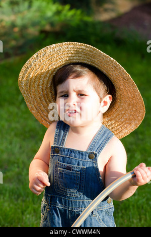 boy with straw hat, a young outfielder playing with a hose Stock Photo