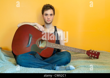 A Young Man sitting on his bed in his bedroom holding his Guitar on his lap. Stock Photo
