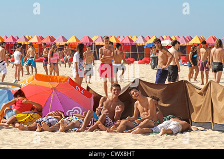 Young men sitting having fun on the beach in Espinho on a sunny summer's day. Colourful beach tents and beach crowd activity, Portugal