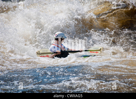 Young caucasian adult male wearing a white crash helmet in a green playboat water kayaking on a the River Ottawa, Canada Stock Photo