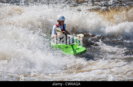 Young caucasian adult male wearing a white crash helmet in a green playboat water kayaking on a the River Ottawa, Canada Stock Photo