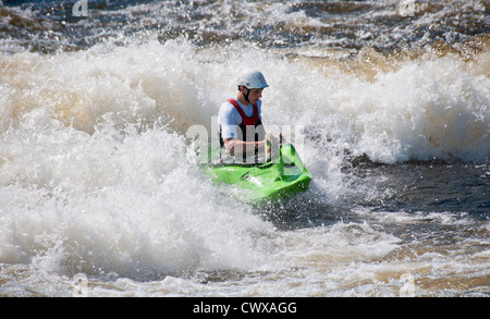 Young caucasian adult male wearing a white crash helmet in a green playboat water kayaking on a the River Ottawa, Canada Stock Photo