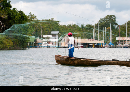 Garifuna fisherman in dugout canoe boat casting fishing net on Lake Izabal, Lago de Izabal, Guatemala. Stock Photo