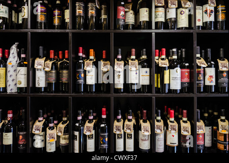 Rows of red wine bottles from local producers adorn shelves in a shop in Cortona, Tuscany, Italy. Stock Photo