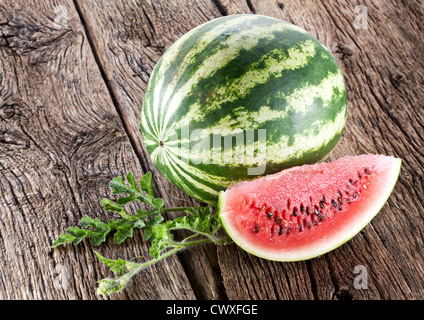 Watermelon with a slice and leaves on a wooden table. Stock Photo