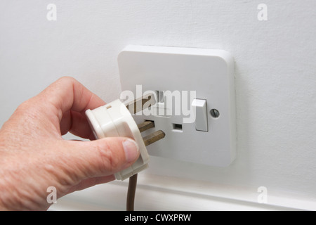 hand putting plug into 3-pin electric socket Stock Photo