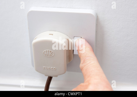 hand putting plug into 3-pin electric socket Stock Photo