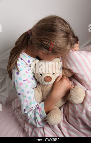 Young girl in bed cuddling a teddy bear. Stock Photo