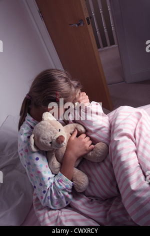 Young girl in bed cuddling a teddy bear. Stock Photo