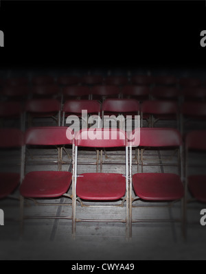 Empty red seating in an auditorium or town hall meeting with rows of old rusting folding chairs in perspective as a symbol of entertainment or performance in politics or performing arts on a blank black background. Stock Photo