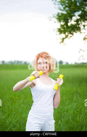 Smiling young woman exercising with dumbbells outdoors Stock Photo