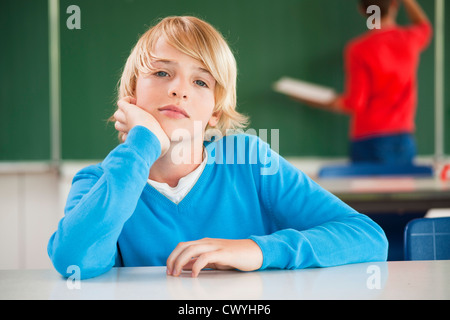 Schoolboy in classroom resting his head in hands, portrait Stock Photo