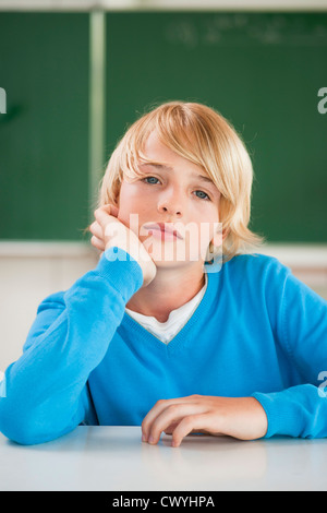 Schoolboy in classroom with hand on chin, portrait Stock Photo