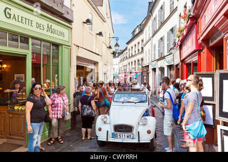 People  walking down a crowded busy street in Montmartre with a citroen 2CV driving past Paris France EU Europe Stock Photo