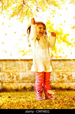 Photo of cute happy small girl standing in autumn park, cheerful sweet female child wearing colorful warm clothes