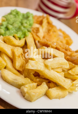 A plate of traditionally fried fish and chips with mushy peas and a mug of tea Stock Photo
