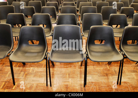 Rows of black plastic chairs in a school hall Stock Photo