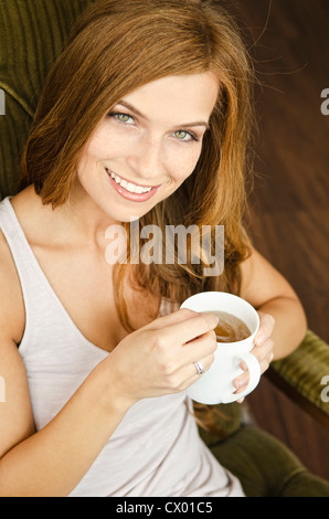 Smiling young woman drinking tea in armchair Stock Photo