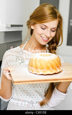 Smiling young woman with cake in kitchen Stock Photo