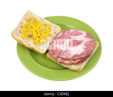 Several slices of capicolla sandwich meat on square bread with mustard on a green plate. Stock Photo