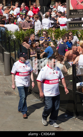 Two Hull Kingston Rovers rugby league football club fans walk past pub beer gardens in  Shambles Square, Manchester. Stock Photo