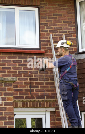 Workman drilling holes in a suburban house wall in preparation for cavity wall insulation Stock Photo