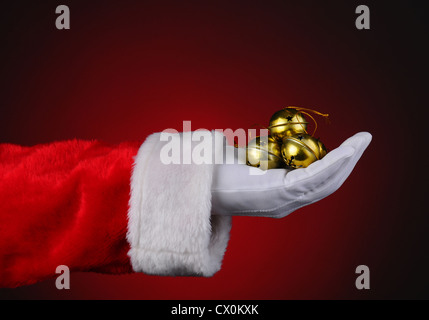 Santa Claus with a handful of gold sleigh bells over a red light to dark background. Stock Photo