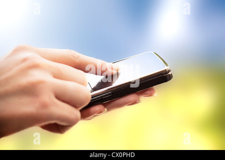 Closeup of female hands using a smart phone. Nature background. Stock Photo