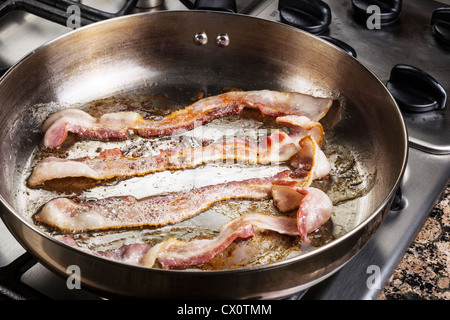 Frying bacon in stainless steel frying pan on stove top Stock Photo