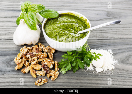 Homemade pesto in bowl with spoon, walnuts, basil, parsley and garlic on aging white ash wood background Stock Photo