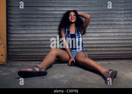 Happy young woman sitting on urban street Stock Photo