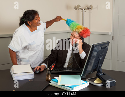 Funny cleaning woman cleaning the office of the manager including his face Stock Photo