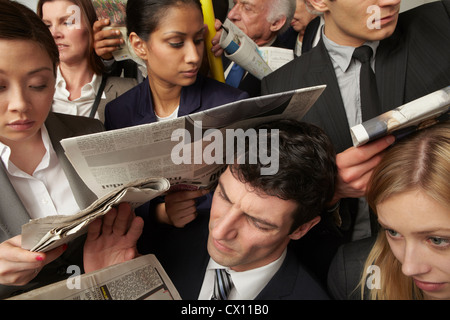 Businesspeople reading newspapers on crowded train Stock Photo