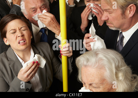 Businesspeople sneezing on subway train Stock Photo