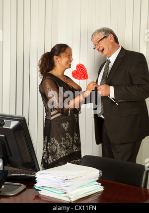 Business manager giving a heart shaped lollipop to his Assistant on Secretary Day Stock Photo