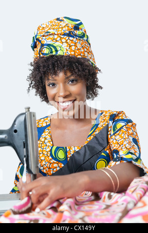 Portrait of an African American woman using sewing machine over gray background Stock Photo