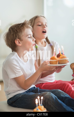 Siblings blowing candles on cupcakes Stock Photo