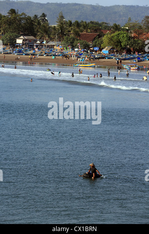 A fisherman paddles a truck inner tube out to sea from a crowded beach in Pangandaran, West Java. Stock Photo
