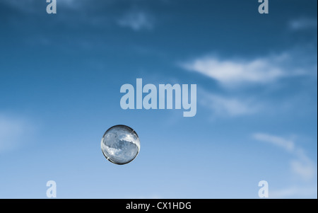 A single soap bubble, reflecting a cottage below, floats up into a blue sky. A journey imagination meditation concept Stock Photo