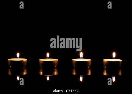 four burning tea candles on a black mirror on black background Stock Photo