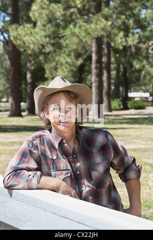 Mature man wearing cowboy hat leaning on wooden slab Stock Photo