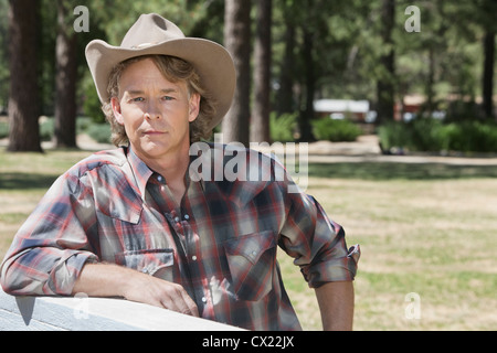 Portrait of a mature man wearing cowboy hat leaning on wooden slab Stock Photo
