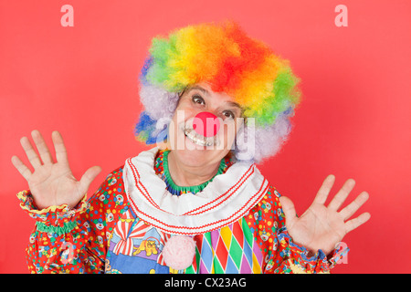 Portrait of funny clown with arms raised against colored background Stock Photo