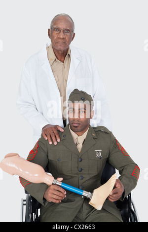 Portrait of senior doctor with US military officer holding artificial limb as he sits in wheelchair over gray background Stock Photo