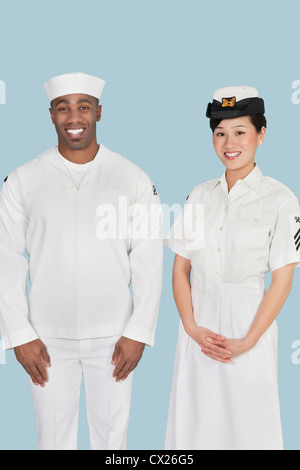 Portrait of happy female US Navy officer with male sailor over light blue background Stock Photo