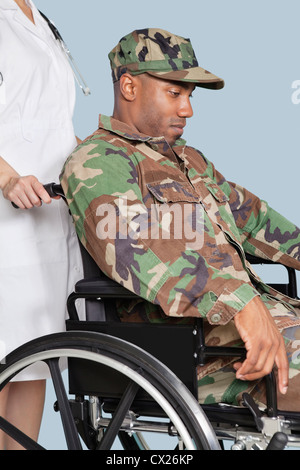 Sad US Marine Corps soldier wearing camouflage uniform in wheelchair assisted by female nurse Stock Photo