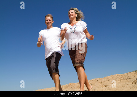 middle aged couple running on beach, background is blue sky Stock Photo