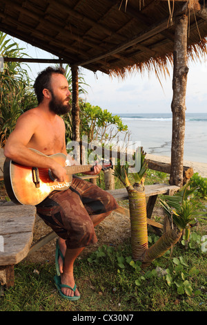 Bearded traveler plays guitar at the beach in West Java, Indonesia. Stock Photo