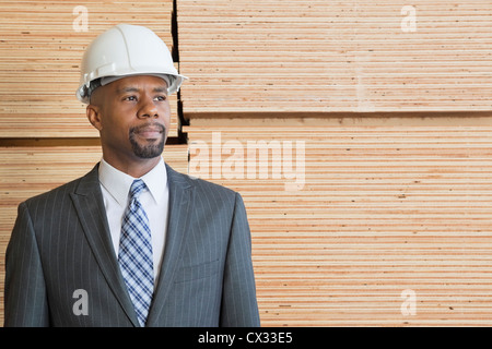 Confident African American male contractor looking away while standing in front of stacked wooden planks Stock Photo